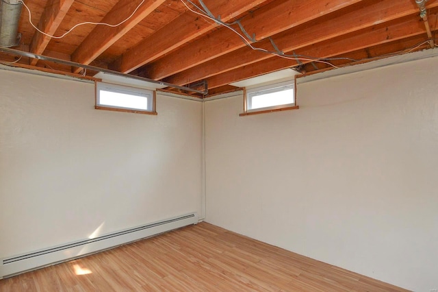 basement featuring wood-type flooring, a baseboard heating unit, and a healthy amount of sunlight