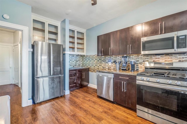 kitchen with appliances with stainless steel finishes, backsplash, light stone counters, dark brown cabinets, and hardwood / wood-style floors