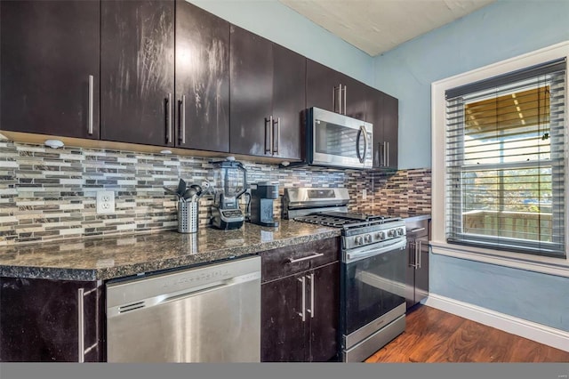 kitchen featuring backsplash, dark wood-type flooring, dark stone countertops, appliances with stainless steel finishes, and dark brown cabinets