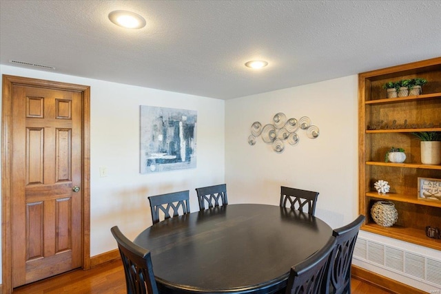 dining room with dark wood-type flooring, a textured ceiling, and radiator heating unit