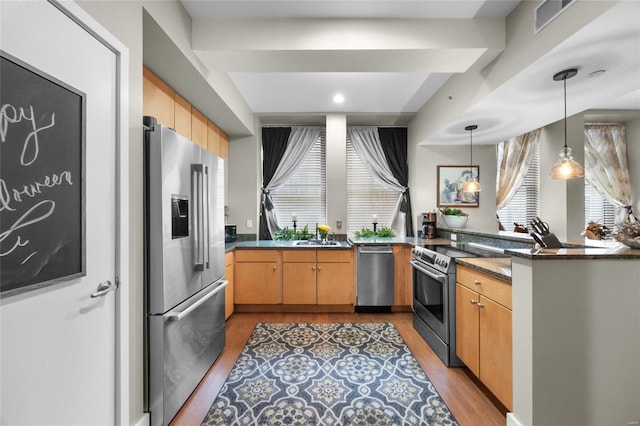 kitchen with kitchen peninsula, appliances with stainless steel finishes, light hardwood / wood-style flooring, dark stone countertops, and pendant lighting