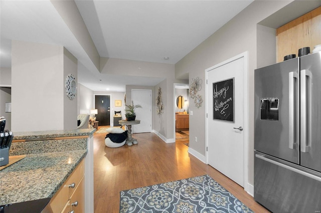 kitchen with light brown cabinets, light hardwood / wood-style flooring, stainless steel refrigerator with ice dispenser, and stone countertops