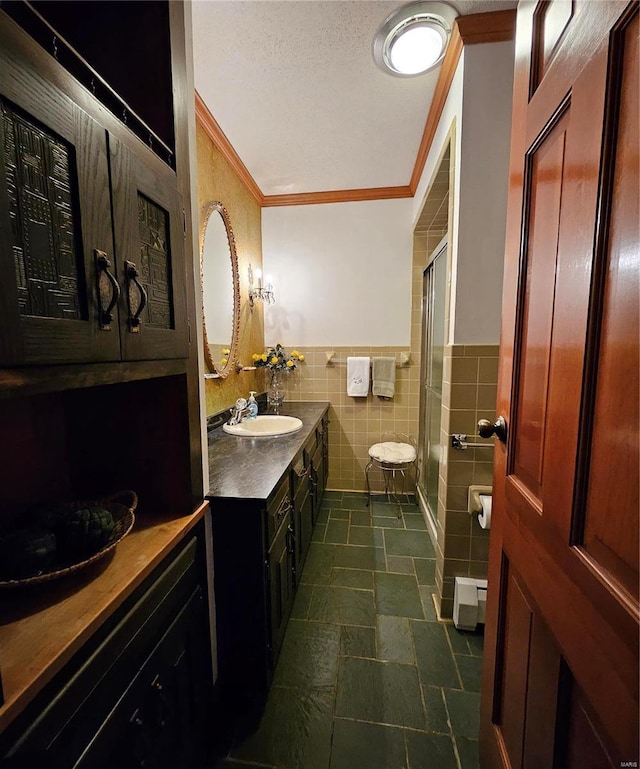 bathroom with vanity, ornamental molding, a textured ceiling, a shower with shower door, and tile walls