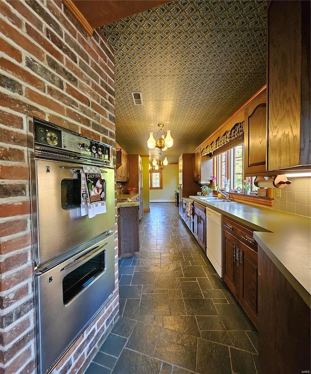 kitchen featuring stainless steel double oven, sink, brick wall, a chandelier, and white dishwasher