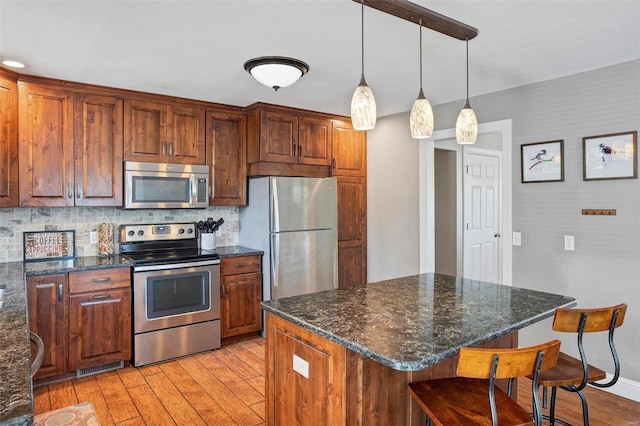 kitchen featuring light hardwood / wood-style flooring, backsplash, a center island, stainless steel appliances, and a breakfast bar