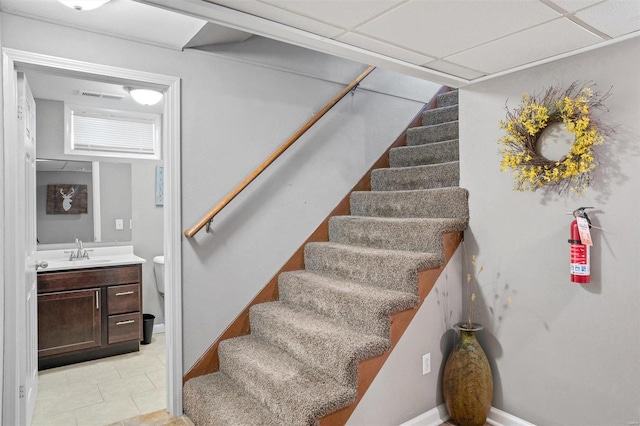 stairs featuring sink, a drop ceiling, and tile patterned flooring