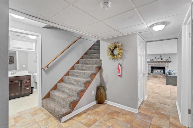 stairway featuring sink, a drop ceiling, a brick fireplace, and tile patterned floors