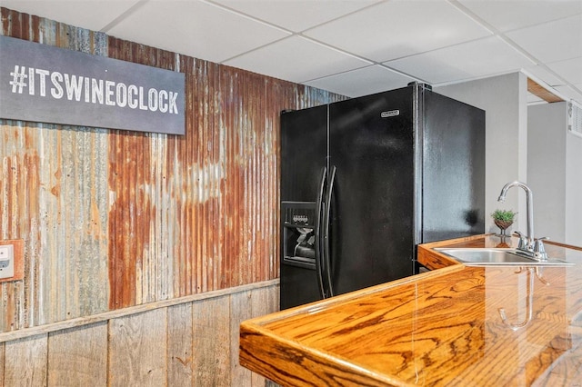 kitchen featuring wood walls, black refrigerator with ice dispenser, and a paneled ceiling