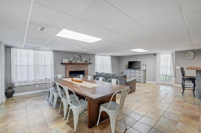 dining room with a drop ceiling, a fireplace, and light tile patterned floors