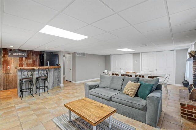 living room featuring a paneled ceiling, wooden walls, bar area, and a brick fireplace