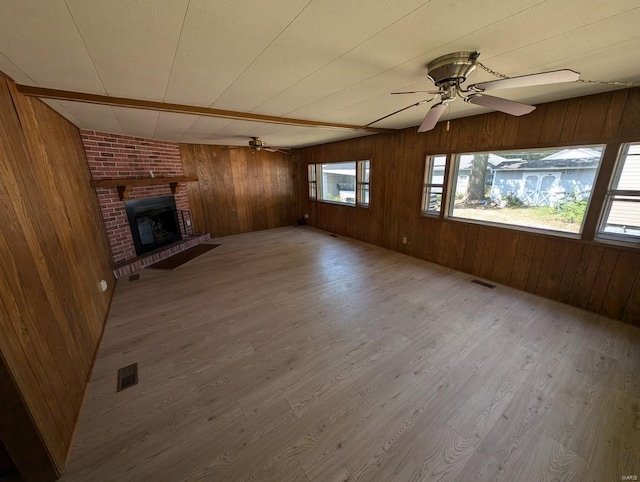 unfurnished living room with wood walls, hardwood / wood-style floors, a fireplace, and ceiling fan