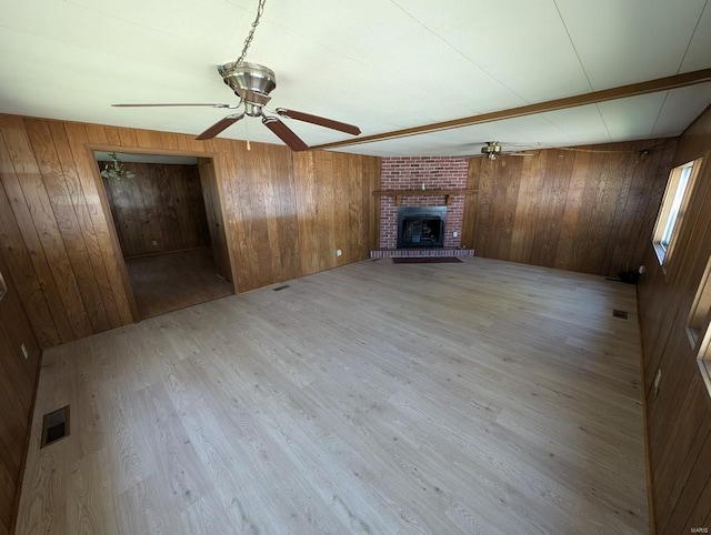 unfurnished living room with a brick fireplace, wooden walls, light hardwood / wood-style flooring, and ceiling fan