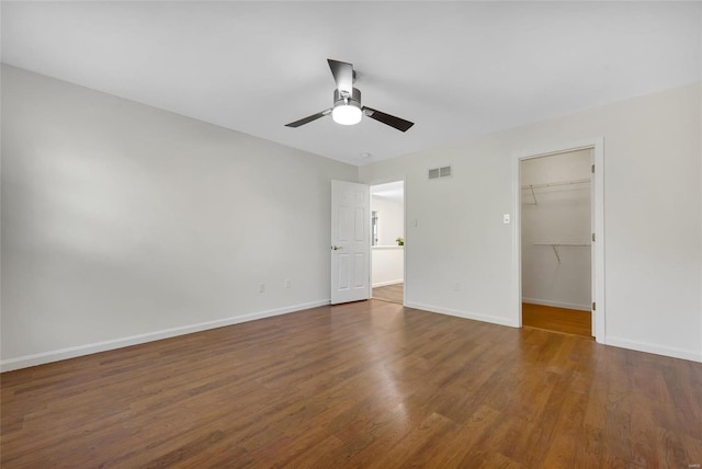 unfurnished bedroom with ceiling fan, a closet, a walk in closet, and dark hardwood / wood-style floors