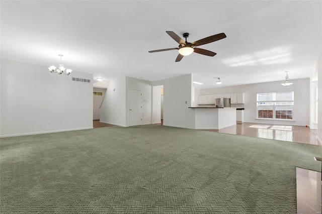 unfurnished living room with ceiling fan with notable chandelier and dark carpet