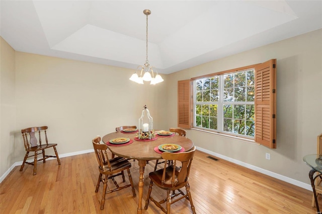 dining space featuring light hardwood / wood-style flooring, a chandelier, and a raised ceiling