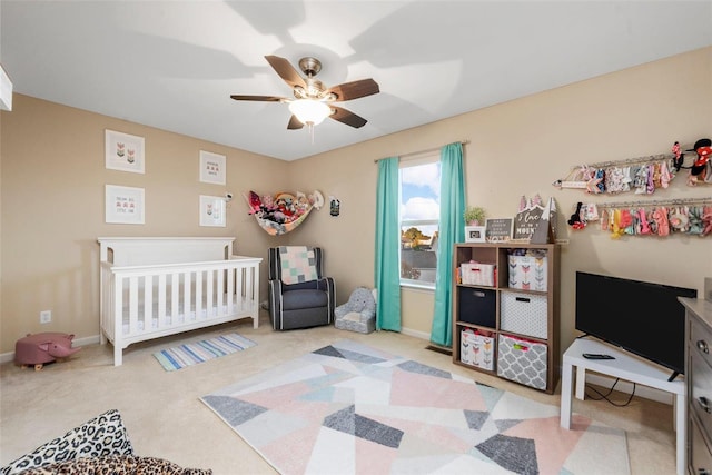 bedroom featuring light carpet, a nursery area, and ceiling fan