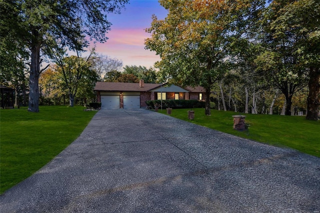 ranch-style home with a garage, a chimney, aphalt driveway, a front yard, and brick siding