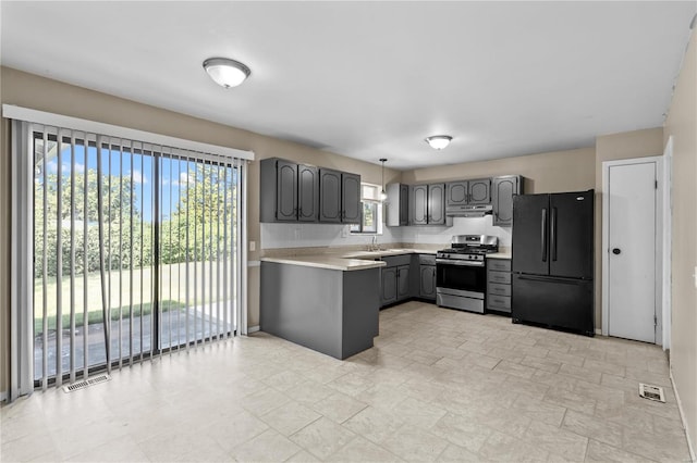 kitchen featuring stainless steel gas stove, hanging light fixtures, black fridge, and gray cabinetry