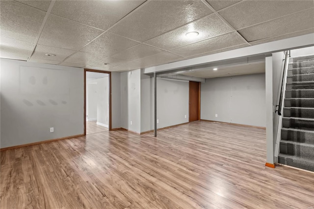 basement featuring a paneled ceiling and light hardwood / wood-style flooring