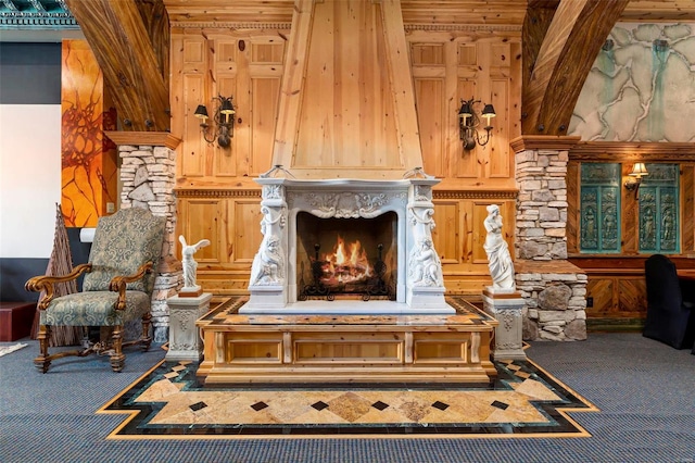 living area with a stone fireplace, carpet, and wooden walls