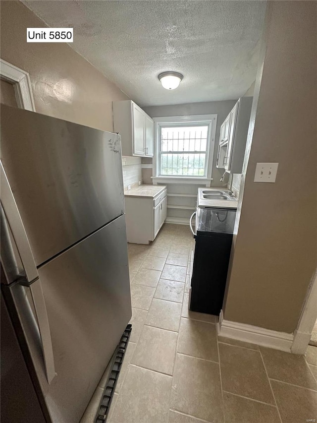 kitchen with sink, light tile patterned floors, white cabinets, a textured ceiling, and stainless steel refrigerator