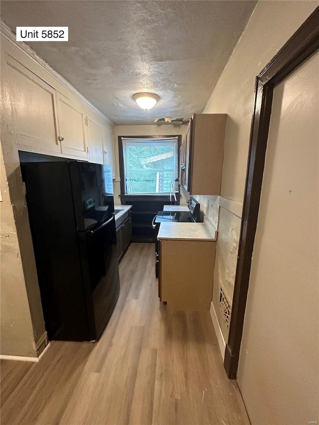 kitchen featuring a textured ceiling, light wood-type flooring, and black fridge