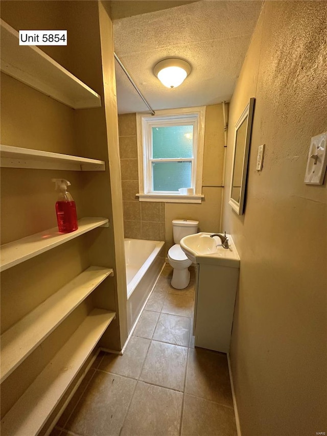 bathroom with vanity, a textured ceiling, toilet, a bathtub, and tile patterned flooring