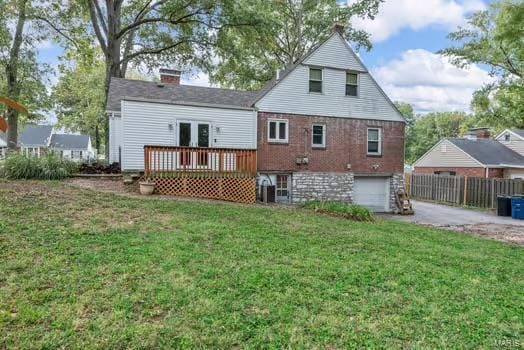 back of property with fence, a wooden deck, driveway, and a yard