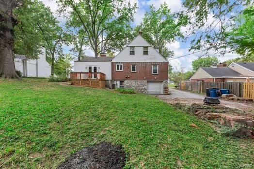 rear view of property featuring a yard, concrete driveway, a deck, an attached garage, and fence