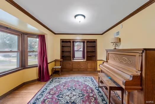 sitting room with baseboards, light wood-type flooring, visible vents, and crown molding