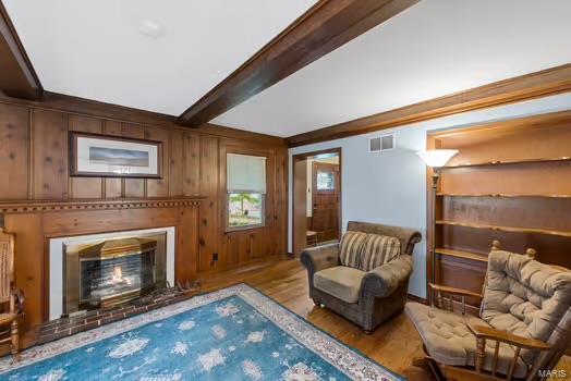 living area with wooden walls, beamed ceiling, light wood-type flooring, and a fireplace