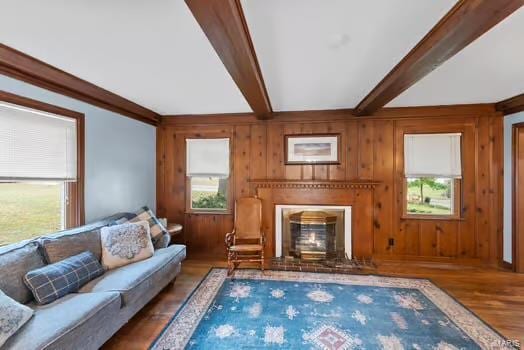 living area with beam ceiling, wood finished floors, wooden walls, and a glass covered fireplace