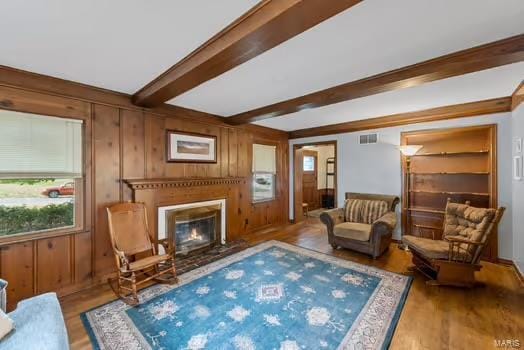 living area with wood finished floors, a glass covered fireplace, beam ceiling, visible vents, and wooden walls
