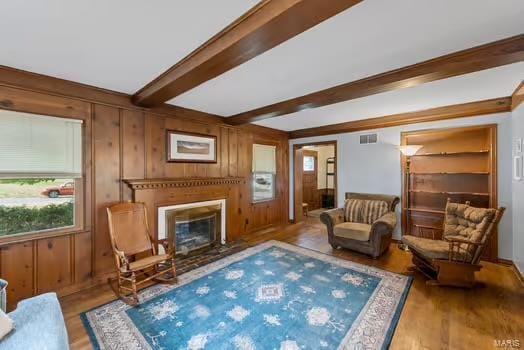 living room with beam ceiling, a wealth of natural light, wood finished floors, and a glass covered fireplace
