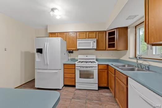 kitchen featuring a sink, glass insert cabinets, white appliances, brown cabinetry, and light countertops