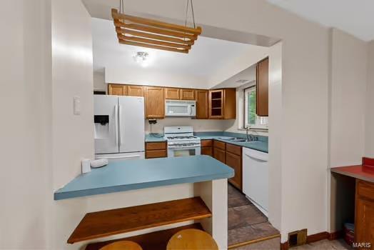 kitchen featuring a kitchen breakfast bar, white appliances, a sink, a peninsula, and brown cabinetry