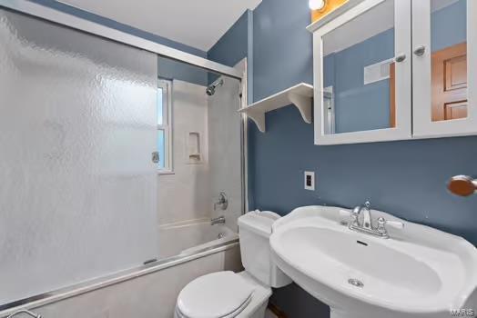 full bathroom with combined bath / shower with glass door, toilet, and a sink