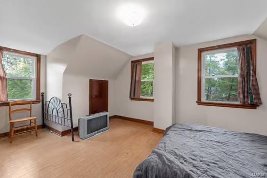 bedroom with baseboards, vaulted ceiling, and light wood-style floors