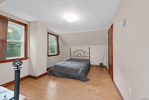 bedroom featuring light wood finished floors, visible vents, lofted ceiling, and baseboards