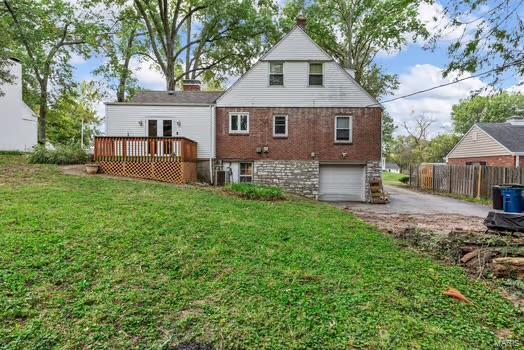 rear view of house with a garage, a lawn, driveway, a deck, and fence