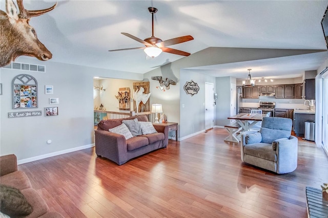 living room with sink, wood-type flooring, ceiling fan with notable chandelier, and vaulted ceiling