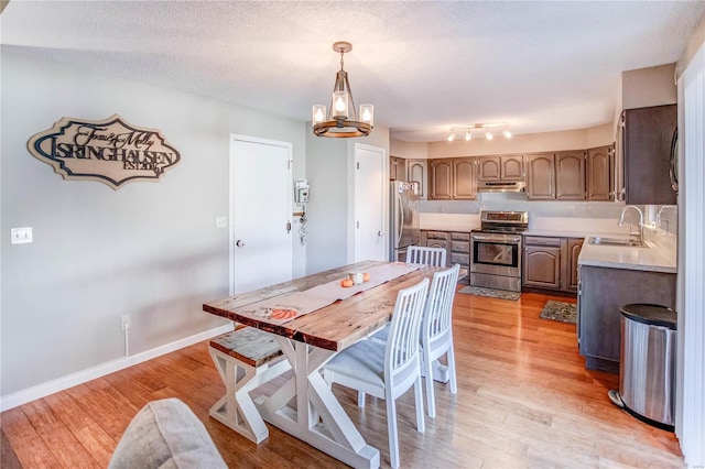 dining area featuring a chandelier, sink, a textured ceiling, and light wood-type flooring