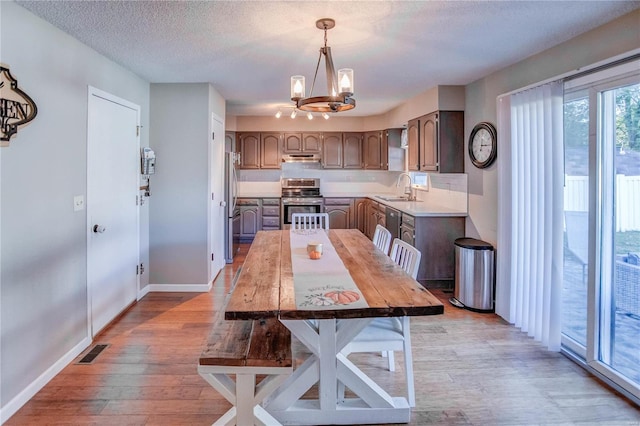 dining area featuring a chandelier, a textured ceiling, sink, and light wood-type flooring