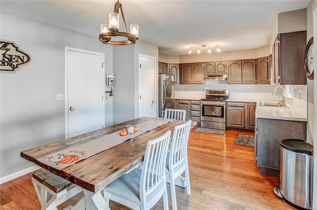 kitchen featuring appliances with stainless steel finishes, sink, a textured ceiling, pendant lighting, and light hardwood / wood-style flooring