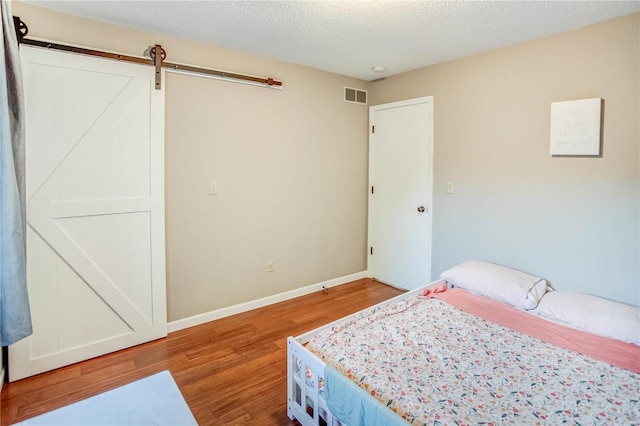 bedroom featuring a textured ceiling, a barn door, and hardwood / wood-style flooring