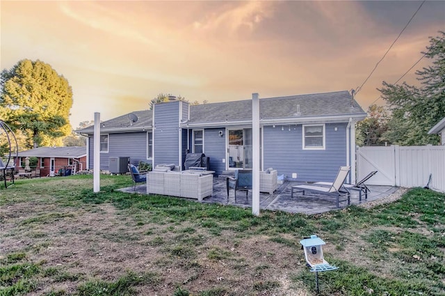 back house at dusk featuring central air condition unit, a patio area, a lawn, and an outdoor hangout area