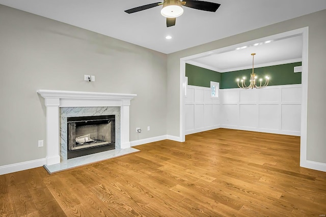 unfurnished living room featuring ornamental molding, wood-type flooring, a fireplace, and ceiling fan with notable chandelier