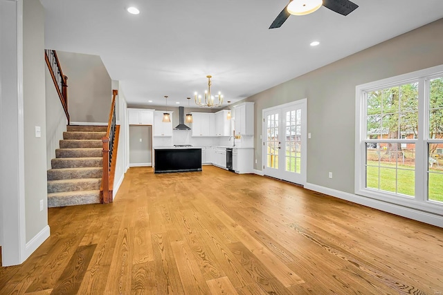 unfurnished living room featuring ceiling fan with notable chandelier, light hardwood / wood-style flooring, and french doors