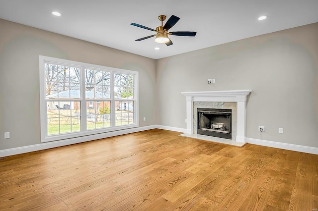 unfurnished living room with ceiling fan, a high end fireplace, and light hardwood / wood-style floors