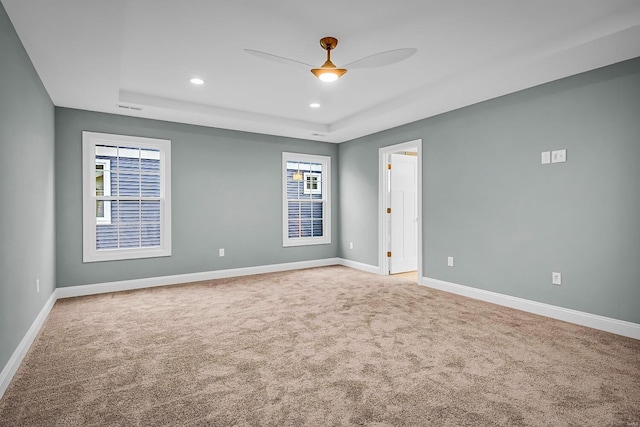 spare room with a tray ceiling, ceiling fan, and carpet flooring